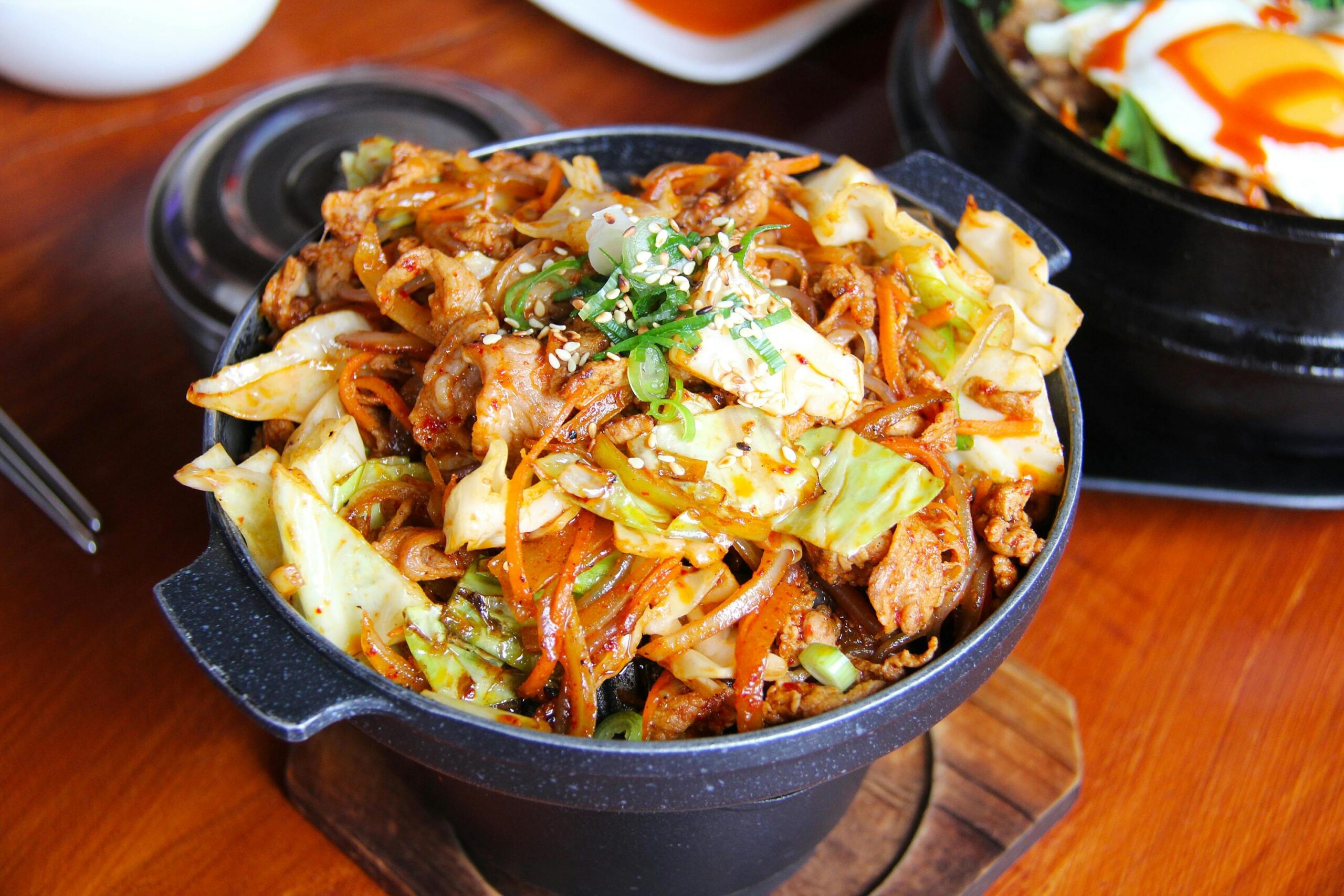 Savory Korean stir-fried noodles with vegetables and meat in a traditional stone bowl.