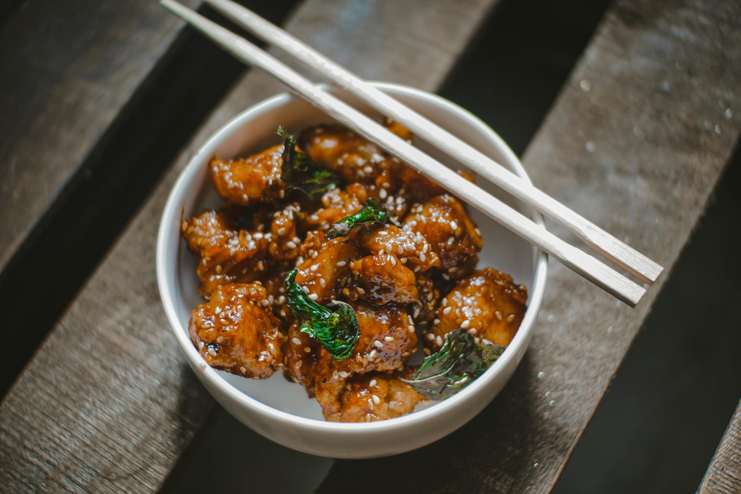 Mouthwatering Korean chicken bowl garnished with sesame seeds and herbs, served with chopsticks.